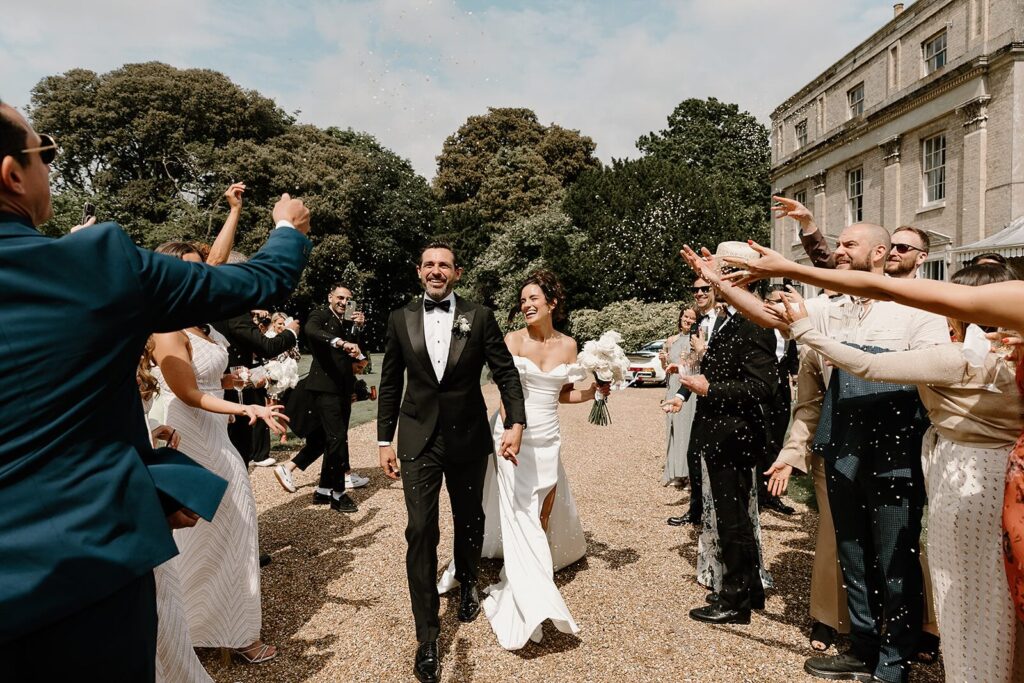Newlywed couple outside Ripple Court Estate with their guests throwing confetti